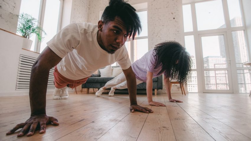 A couple performs push-ups together in a bright, modern home setting, emphasizing fitness and unity.